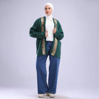 Woman wearing a green cardigan with gold trim, white shirt, and blue pants on a white background