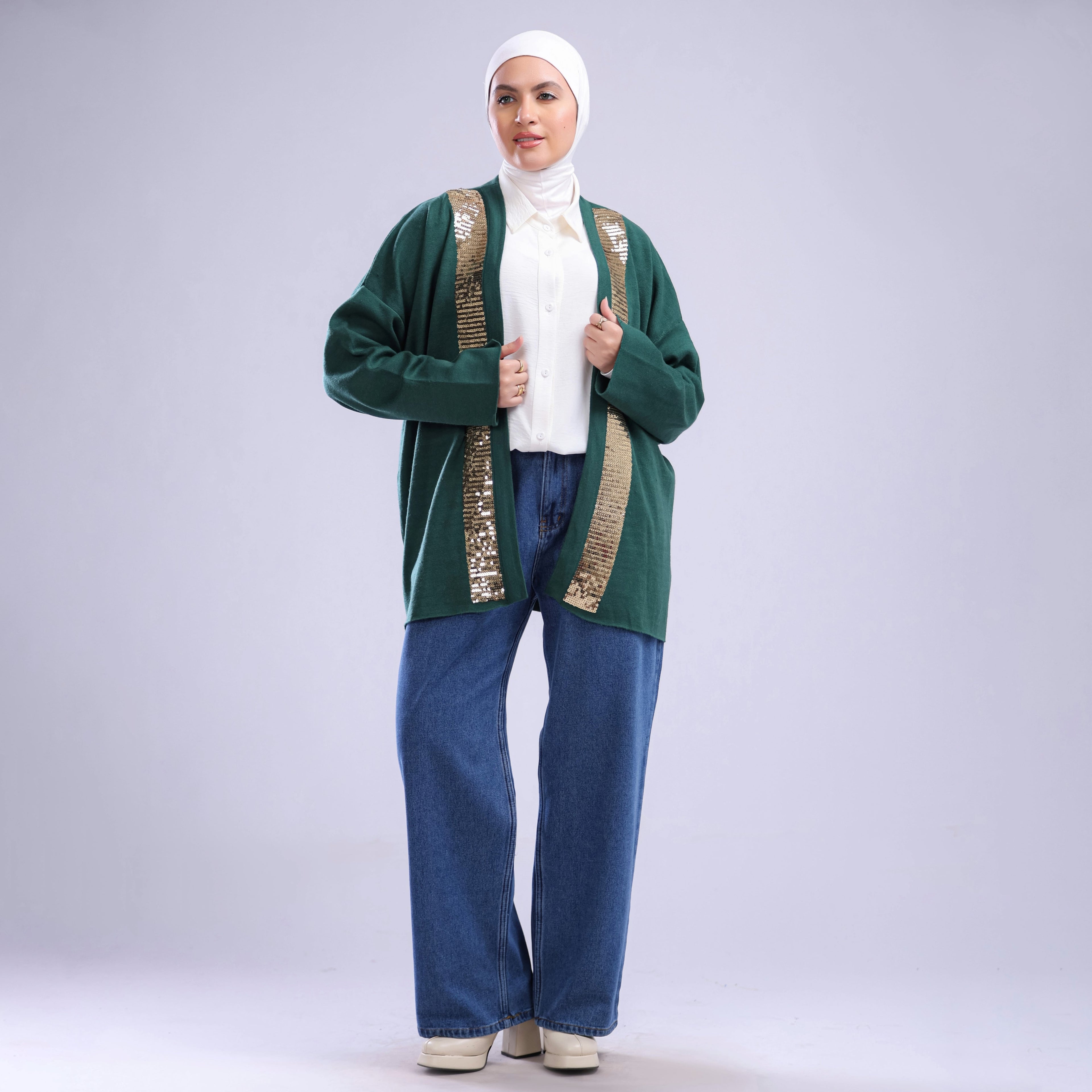 Woman wearing a green cardigan with gold trim, white shirt, and blue pants on a white background